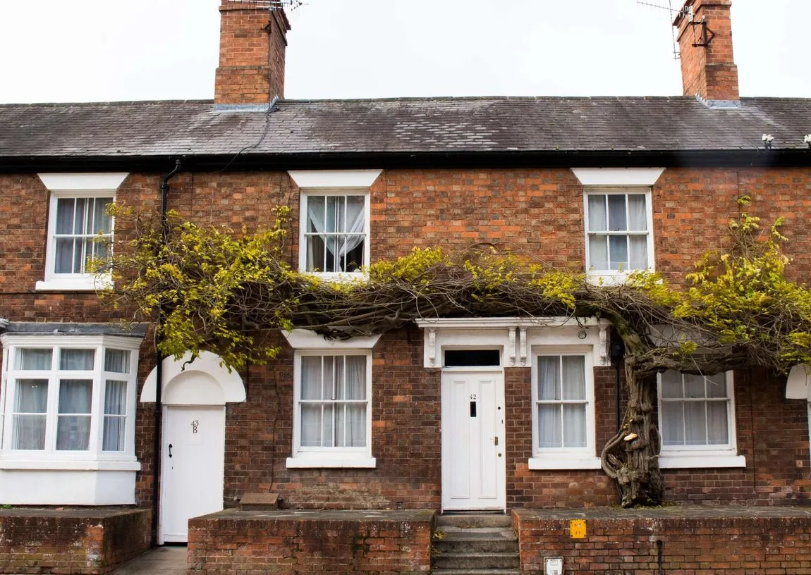 Victorian red-brick terraced house with its original white timber windows and white front door, photographed from the street